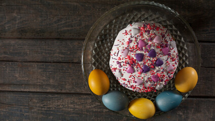 Easter cake in a transparent dish, around painted eggs in the colors of the flag of Ukraine. Yellow and blue (cyan). On wood texture. Concept: food, holiday, war in Ukraine