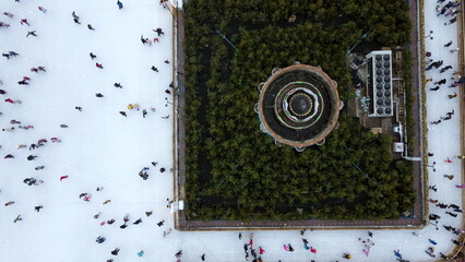 Aerial Drone View Flight Over many people in colorful clothes skating on open-air ice rink in winter. Urban Ice skating top view. City Park, Publik Ice Rink. Winter outdoor. Skating sport background