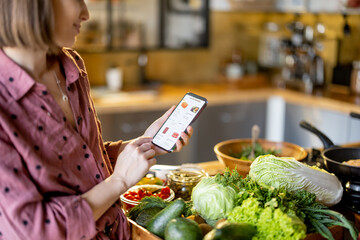 Young housewife shopping groceries online on mobile phone, close-up on phone screen with e-shop and food on background