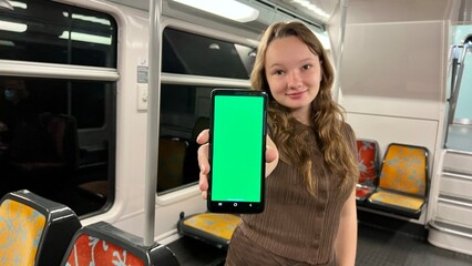 A teenager girl holds a green screen with a chroma key in her hands, dances, smiles, looks into the frame, shows class and is very pleased she is alone in the train rides sunny on the street 4k video