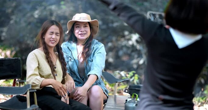 Handheld shot, Young pretty taking photo by camera two female friends while sitting at the camping tent with bonfire in forest on holiday vacation, Young Asian group woman travel outdoor camping.