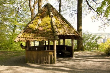 Die Zauberhafte Raststätte beim Hexenplatz in Brugg. Die Bänke zum ausruhen sind von einem spitz zulaufenden, moosbewachsenen Dach geschützt.