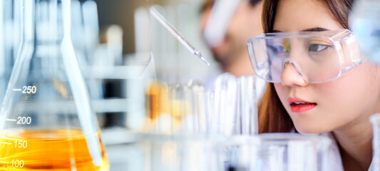 Attractive scientist woman looking chemical sample in flask at laboratory with lab glassware background. Science or chemistry research and development concept.