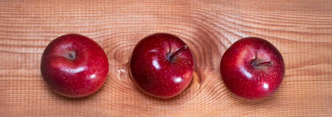 Top view banner with three red apples on a wooden background with a place for text: rustic food, harvest gardening, ingredients for a healthy snack, soft focus