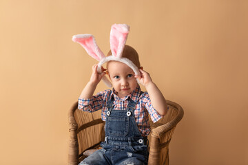 Cute little boy with bunny ears on beige background. Happy Easter