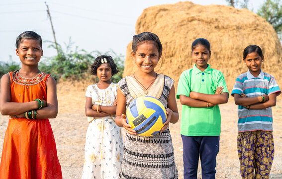 group of Indian village girls with one child holding football by looking at camera during training - concept of positiv emotion, training and hobbies