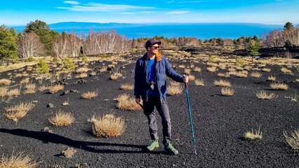 Tourist man with hiking pole and camera at crater of Sartorio on volcanic landscape of volcano...