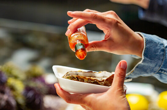 Unrecognizable girl with an oyster pouring hot sauce on it at the Paris market, Boulevard Richard Lenoir in Bastille, Paris (France), selective focus on the right hand.