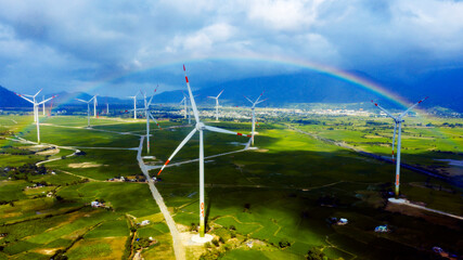 Wind turbine towers in a green field under the blue sky with rainbow generating alternative energy...