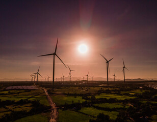 Wind farm or wind park, with high wind turbines in the setting sun for generation electricity with...