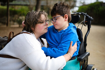 Disabled boy in a wheelchair and his mother enjoying a day together outdoors in a park.