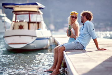 Couple toasting with beer sitting by water on wooden jetty. Couple in love. Holiday, lifestyle,...