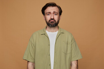Fototapeta premium studio portrait of bearded man posing over beige background looking into camera with sad, depressed facial expression
