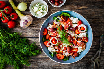 Tasty salad - prosciutto di Parma, feta cheese, cherry tomatoes, black olives and fresh, green vegetables on wooden table 