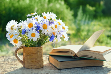 flowers bouqet in cup and old books on table in garden. rustic summer natural background. concept of reading, relaxation. summer season - obrazy, fototapety, plakaty