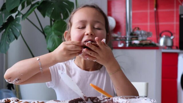 Portrait of happy little girl is dancing while decorates homemade gingerbread with chocolate icing and eating it, 4K footage