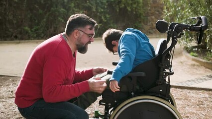 A father playing and having fun with his son with disabilities in wheelchair while enjoying time together outdoors. - Powered by Adobe