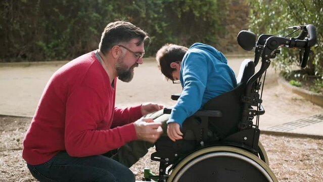 A father playing and having fun with his son with disabilities in wheelchair while enjoying time together outdoors.