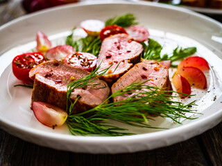 Roasted pork loin slices with dill and cherry tomatoes on wooden table