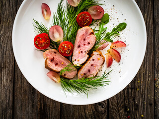 Roasted pork loin slices with dill and cherry tomatoes on wooden table