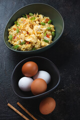 Bowl of chinese fried rice mixed with chicken eggs, vertical shot on a dark-brown stone background, selective focus