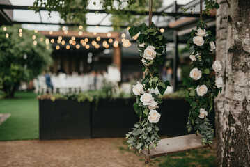 Swing decorated with white flowers hanging on tree in garden.