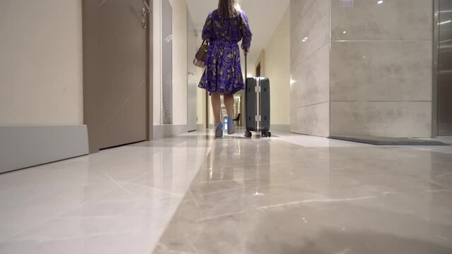 An elegant businesswoman with luggage on trolley in lobby of hotel. female executive or traveler with a suitcase on a business trip related to work is walking down the corridor of the hotel