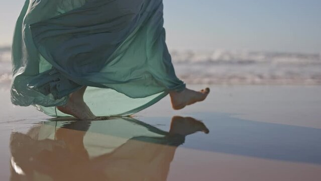 Slow motion shot of woman feet walk along ocean beach. Woman in long flowing dress walks along the ocean. UHD, 4K.
