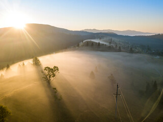 The rays of the morning sun through the fog in the mountains. Aerial drone view.