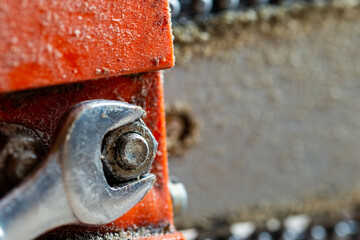 Shiny wrench tightening the bolt on a dusty old chainsaw close up macro shot, space for text.