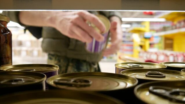 Close-up of many beautiful tin cans on a supermarket shelf and a man with a shopping trolley takes one