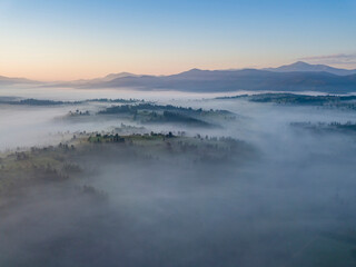 Flight over fog in Ukrainian Carpathians in summer. Mountains on the horizon. Aerial drone view.
