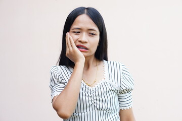 Asian woman with toothache presses her hand to her face	