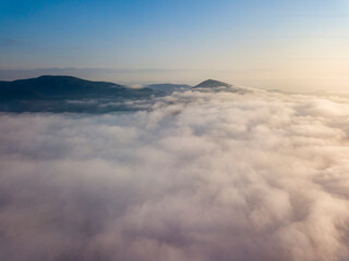 Flight over fog in Ukrainian Carpathians in summer. Mountains on the horizon. Aerial drone view.