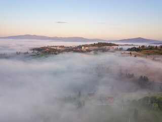 Mountain settlement in the Ukrainian Carpathians in the morning mist. Aerial drone view.