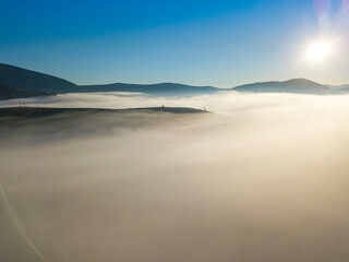 Flight over fog in Ukrainian Carpathians in summer. Mountains on the horizon. A thick layer of fog covers the mountains with a continuous carpet. Aerial drone view.