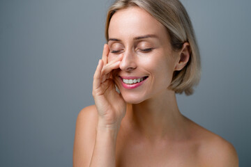 Skin care. Blonde woman with beauty face touching healthy facial skin. No makeup. Grey background.