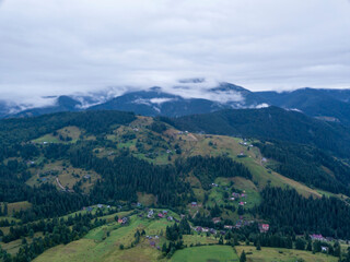 Green slopes of Ukrainian Carpathian mountains in summer. Cloudy morning, low clouds. Aerial drone view.