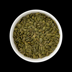 bowl of green pumpkin seeds on black background, top view
