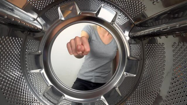 chamber is inside drum of washing machine. woman's hand shows fig and an obscene gesture, fuck you. woman puts her hand inside and shows that she is tired of doing laundry and cleaning. wants to rest