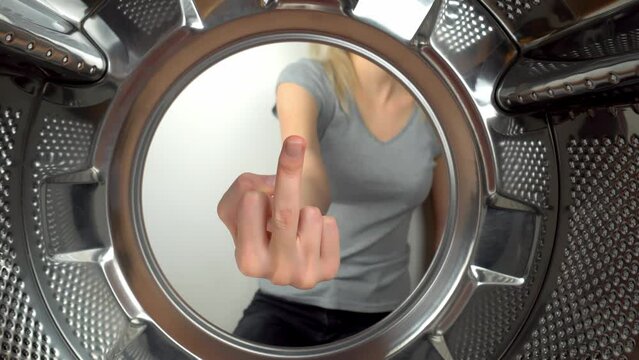 chamber is inside drum of washing machine. woman's hand shows fig and an obscene gesture, fuck you. woman puts her hand inside and shows that she is tired of doing laundry and cleaning. wants to rest