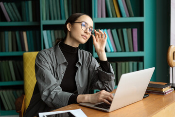 A modern woman with glasses designer works in an office, uses a computer tablet, communicates online with a client.