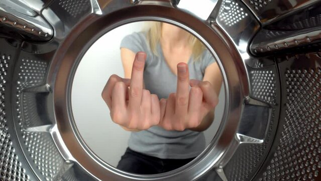 chamber is inside drum of washing machine. woman's hand shows fig and an obscene gesture, fuck you. woman puts her hand inside and shows that she is tired of doing laundry and cleaning. wants to rest