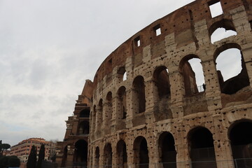 Fototapeta premium ROME, ITALY - February 05, 2022: Panoramic view around the Colosseum in city of Rome, Italy. Cold and gray sky in the background. Macro photography of the green parks with the old buildings.