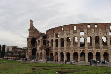 Fototapeta premium ROME, ITALY - February 05, 2022: Panoramic view around the Colosseum in city of Rome, Italy. Cold and gray sky in the background. Macro photography of the green parks with the old buildings.