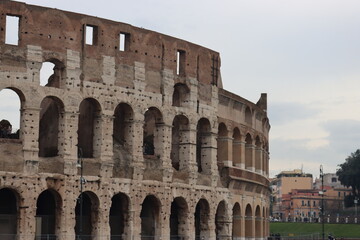 Fototapeta premium ROME, ITALY - February 05, 2022: Panoramic view around the Colosseum in city of Rome, Italy. Cold and gray sky in the background. Macro photography of the green parks with the old buildings.
