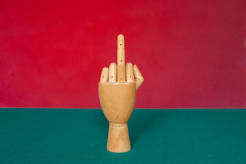 Wooden hand with middle finger on red-green background