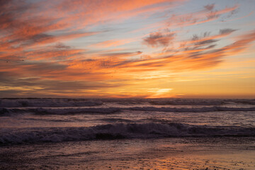 Orange sunset, with birds flying and big waves on Concón beach, Chile