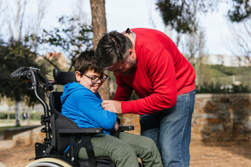 Father playing with his son with disability in a wheelchair while they enjoy time together outdoors...