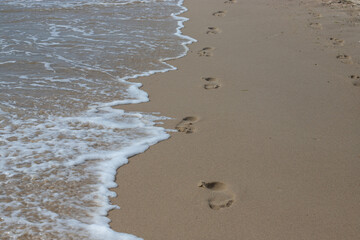Footprints in the sand beach. Footprints in the sand against a sea wave. Footprints on a sunny day with golden sand, beach, wave and footsteps